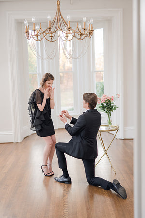 groom on one knee proposing to surprised bride wearing chic modern little white dress with flattering flounce