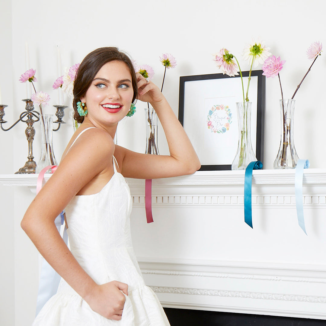 bride wearing short white bridal shower dress with ribbon tie flowers on mantle and colorful ribbons