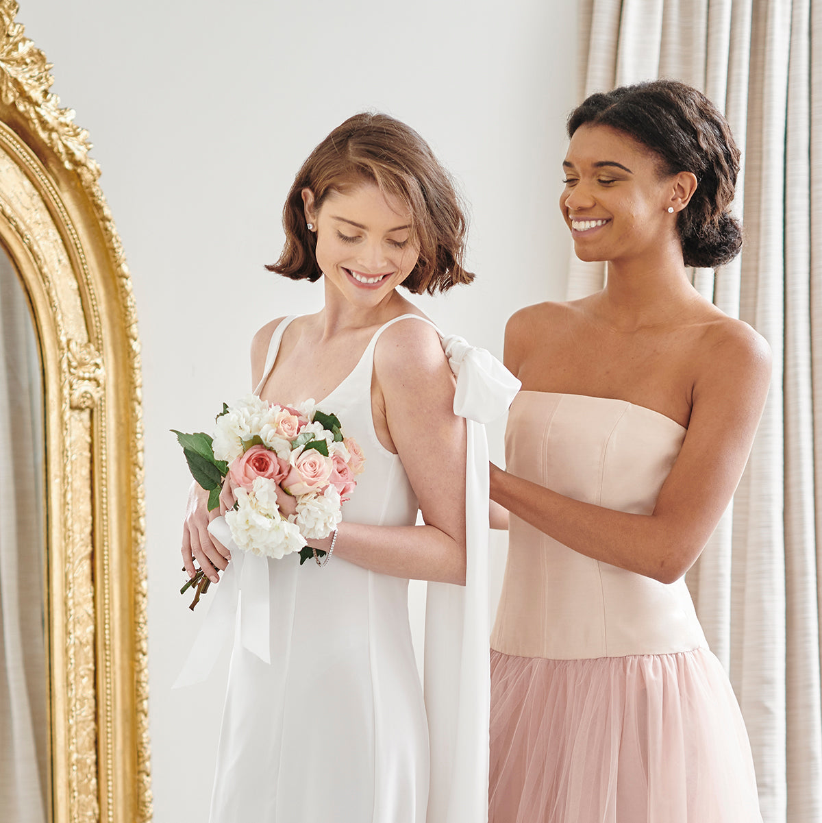 Beautiful happy bride wearing elegant white wedding gown with maid of honor in blush pink tulle bridesmaid wedding dress