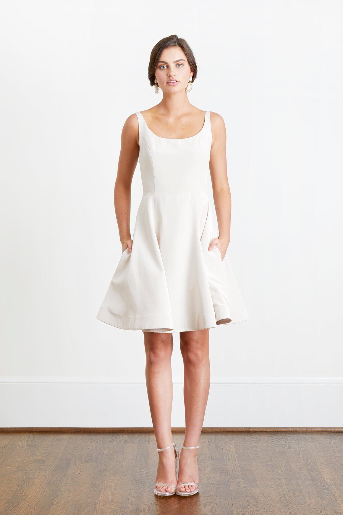 Bride with hands in pockets wearing backless off white cocktail dress