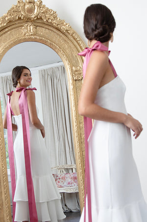 Beautiful bride in white midi wedding rehearsal dinner and reception dress with Barbie Pink straps in mirror