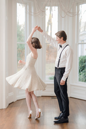 Bride wearing simple elegant designer short strapless sequin mini wedding reception dress twirling during the first dance with groom
